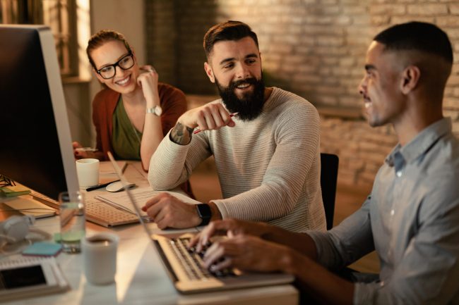 Young entrepreneurs working late and communicating in the office. Focus is on man with beard.